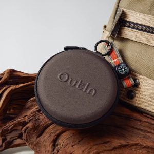 Кръгъл кафяв калъф Outin, бежова чанта с каишка и черен часовник, който лежи върху плаващи дървета.