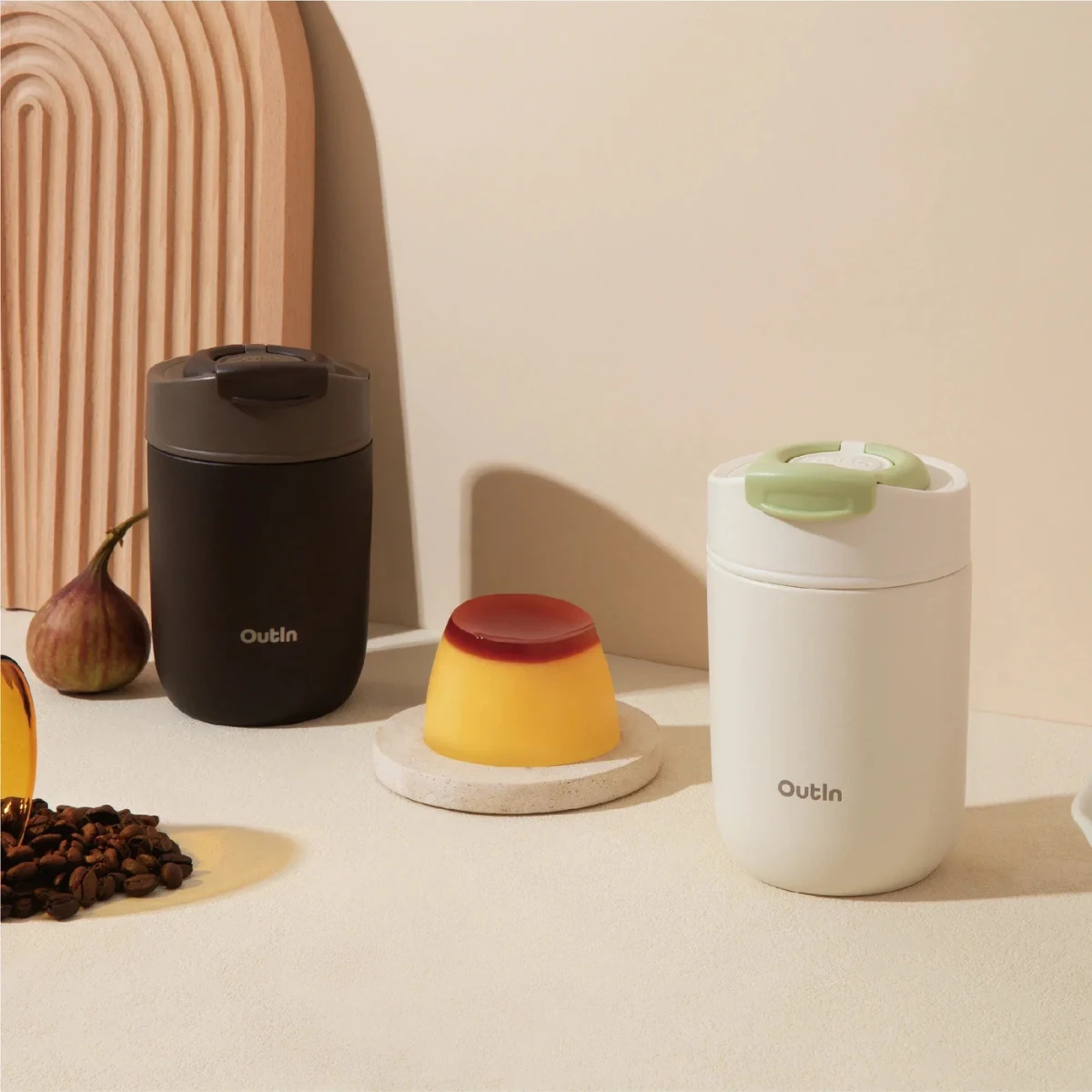 Две чаши Outin Travel Tumblers, черни и бели, са разположени до фланела, кафе на зърна и смокиня върху бежова повърхност. Две чаши Outin Travel Tumblers, черни и бели, са разположени до фланела, кафе на зърна и смокиня върху бежова повърхност.