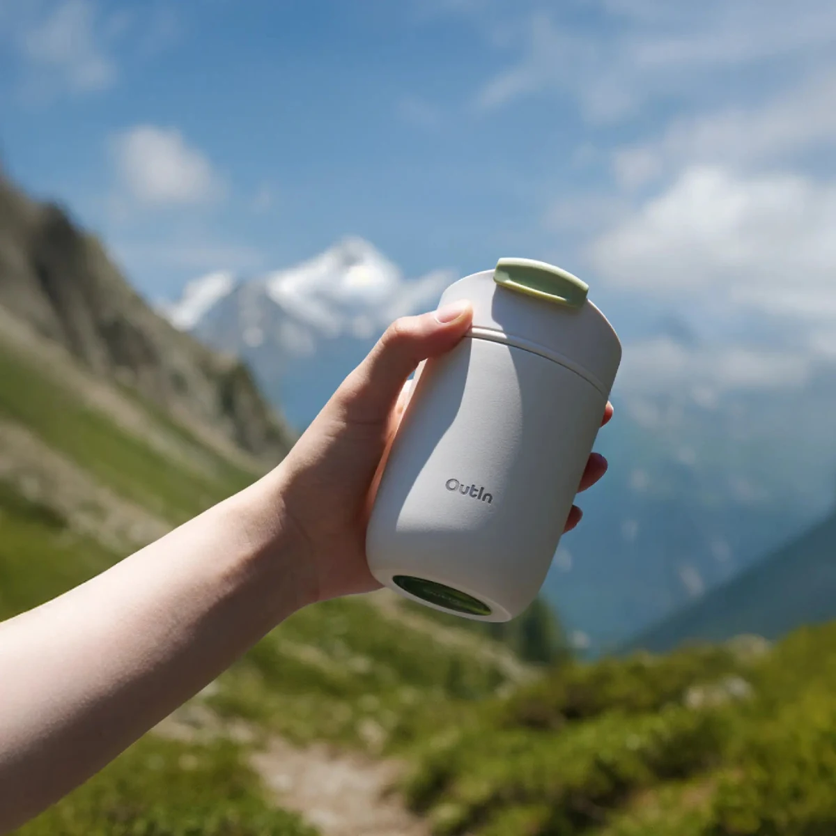 Ръка държи Термочаша Outin Travel Tumbler на открито с планини и синьо небе на заден план. Ръка държи Термочаша Outin Travel Tumbler на открито с планини и синьо небе на заден план.