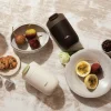 Две чаши Outin Travel Tumblers със смокини, бисквити, кафе на зърна и маракуя върху керамични чинии. Две чаши Outin Travel Tumblers със смокини, бисквити, кафе на зърна и маракуя върху керамични чинии.