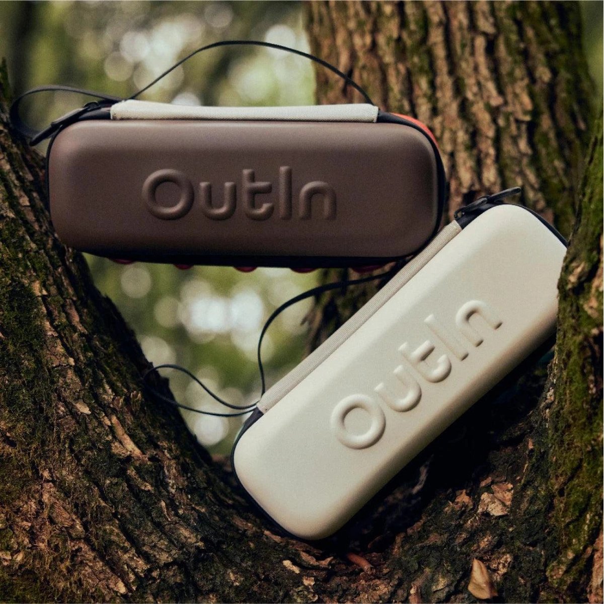 Outin Nano predpazen kaluf eva (8) Два правоъгълни калъфа с марка Outln и Outin, един кафяв и един бежов, са поставени във вилицата на едно дърво.